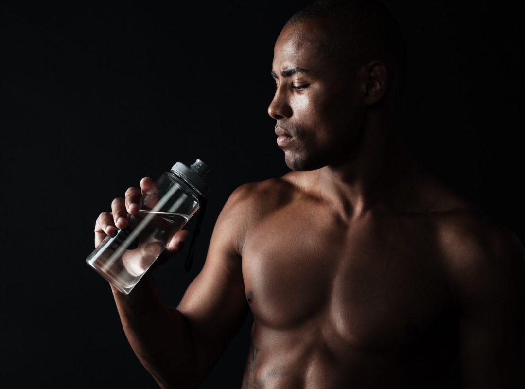 Portrait of tired young afro american sports man, holding bottle of water, over black background
